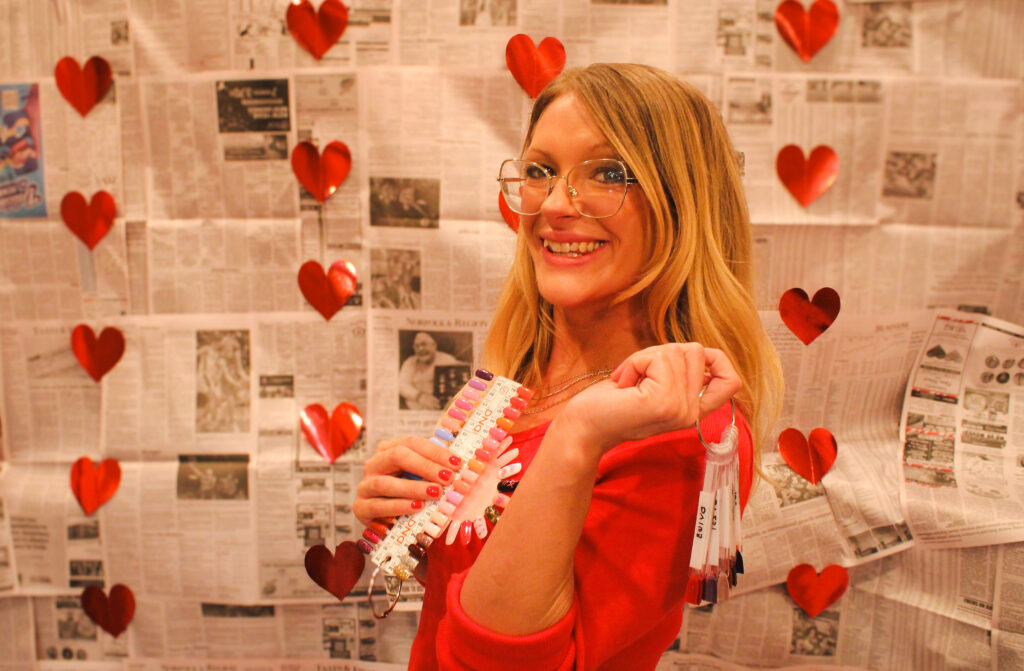 Smiling woman with heart backdrop and glasses.